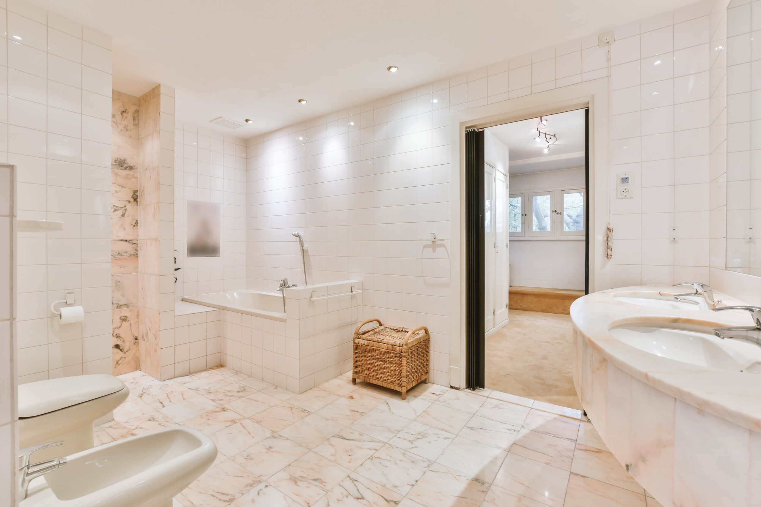 Spacious modern bathroom featuring white tile walls, pink-veined marble floors, a built-in bathtub, and a curved double marble vanity.