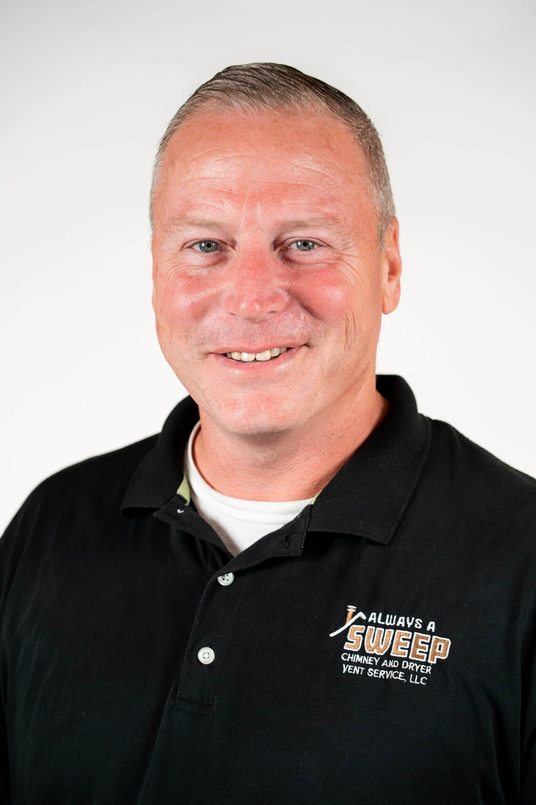 A professional headshot of a smiling man wearing a black polo shirt featuring the "Always a Sweep Chimney and Dryer Vent Service, LLC" logo against a white background.