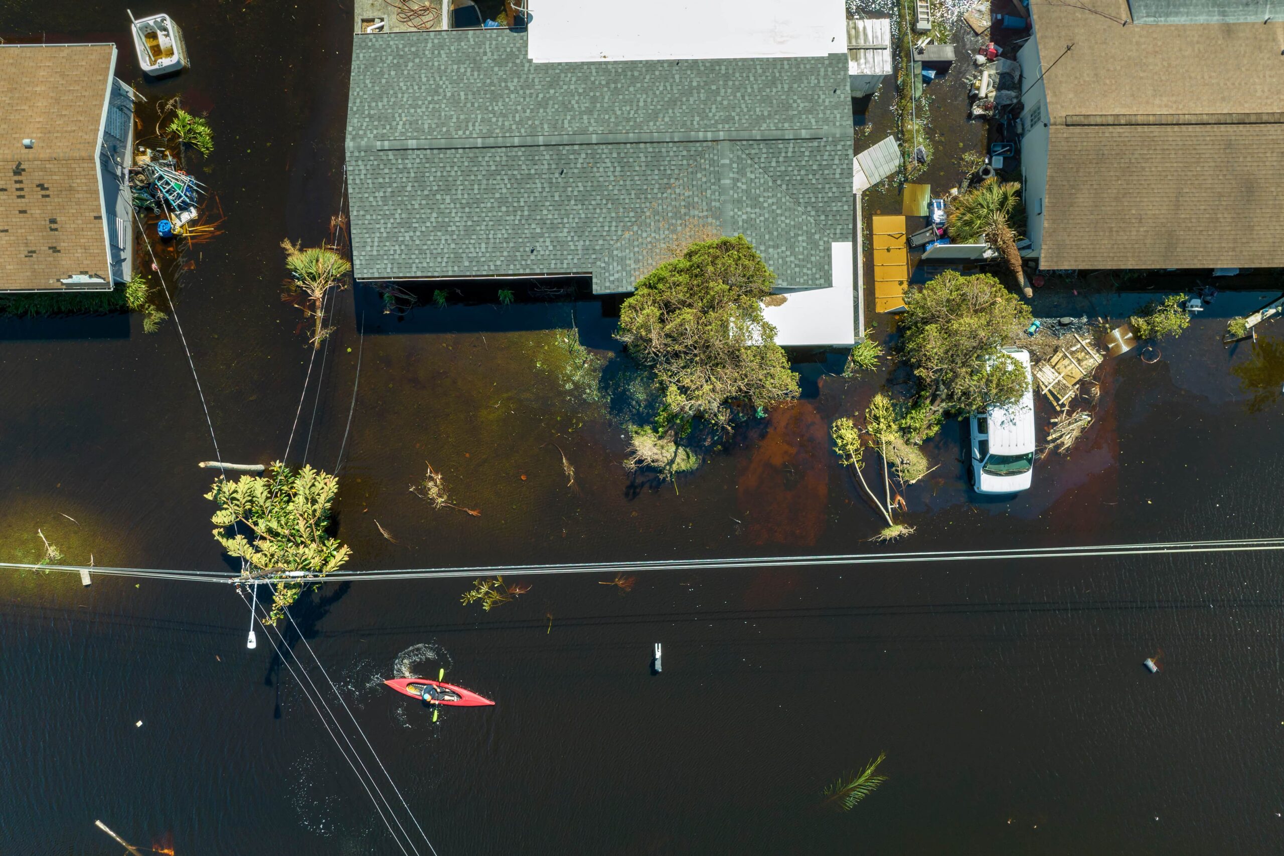 DIY Flood Repair Ocala & Gainesville | Why DIY Restoration Fails in Florida 1 An aerial drone view of a flooded residential street with dark water surrounding houses and a person navigating a red kayak past submerged power lines.