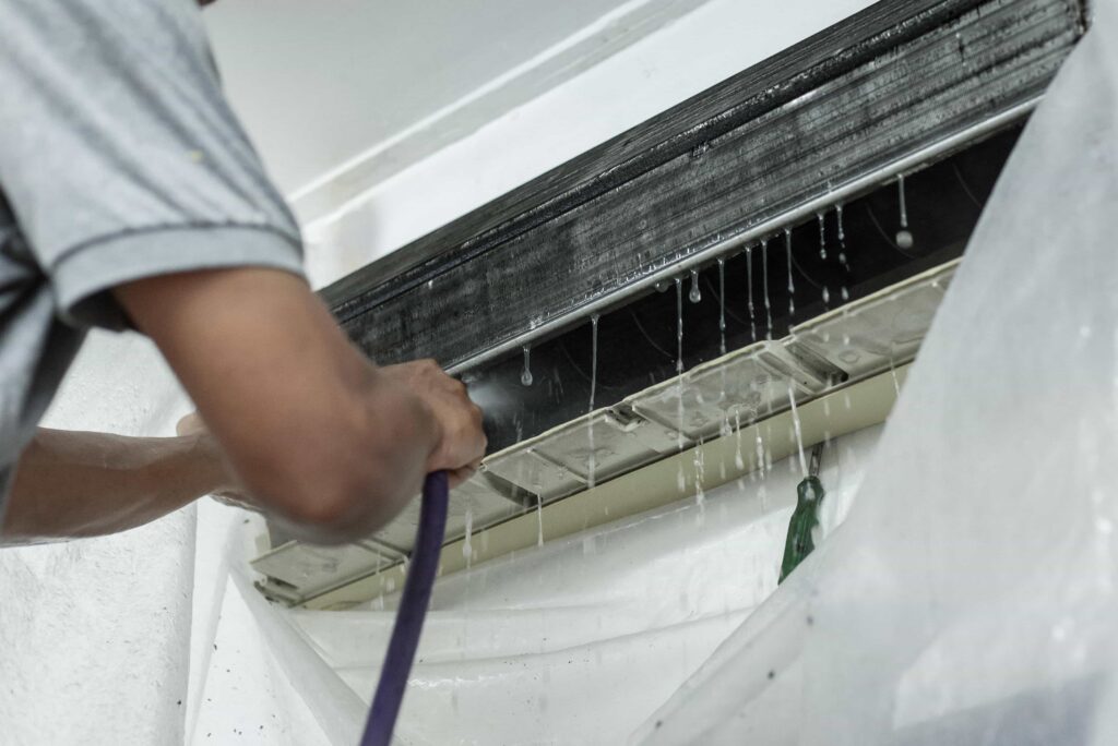 A technician using a water hose to deep clean the evaporator coils of an indoor mini-split air conditioner unit, showcasing professional AC coil cleaning service in Miami, Florida.