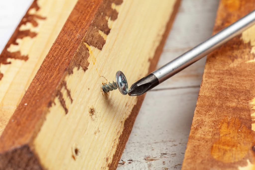 5 Structural Weaknesses in Residential Decks (2026 Guide) 2 A close-up shot of a Phillips head screwdriver turning a metal screw into weathered wooden planks during a residential deck repair denver co project.