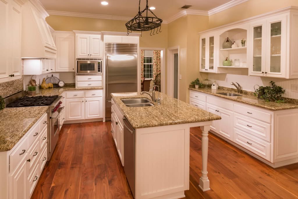 A beautifully renovated kitchen with an island, granite countertops, white cabinetry, and rich hardwood floors, illustrating high-end finishes that influence the kitchen remodel cost in Ocala.